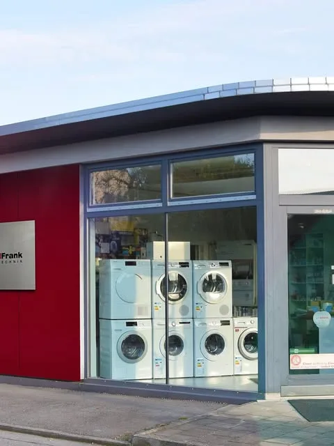 Das Schaufenster mit Waschmaschinen und Trocknern, links an der roten Fassade das Firmenschild