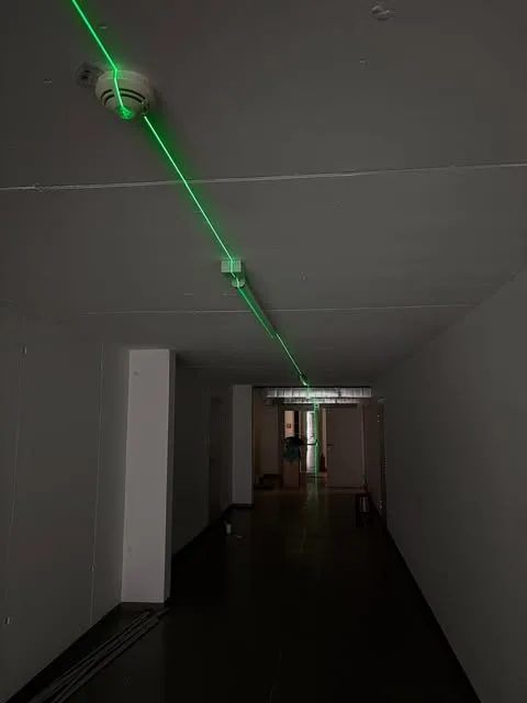 Gang im Rohbau, an der Decke ein Rauchmelder und eine grün leuchtende Laserlinie entlang der Leitungsführung