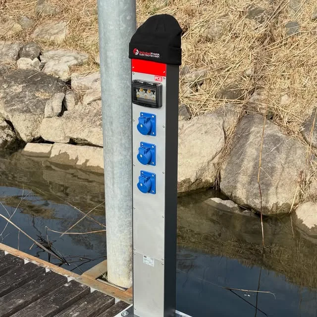 Fertig montierte Stromverteilersäule an einem Holzsteg am Wasser mit drei blauen CEE-Steckdosen